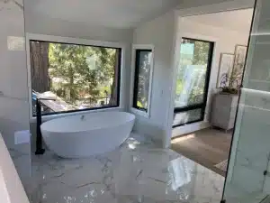 Contemporary bathroom featuring a freestanding tub, black fixtures, marble-look tile floors, and adjacent dressing area