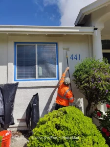 Worker in safety jacket cleaning exterior wall near window and house number 441 on a sunny day