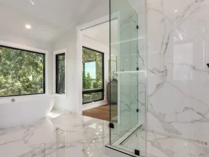 Modern bathroom with glass walk-in shower, marble tile walls, freestanding bathtub, and large windows