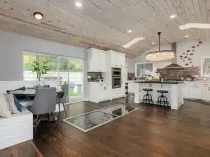 Open-concept kitchen and dining area with white cabinets, wood plank ceiling, island seating, and dark hardwood floors