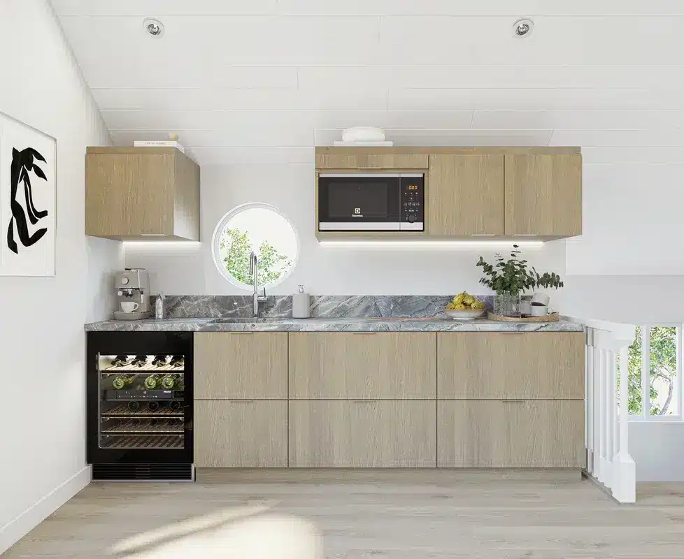 A modern kitchen features light wood cabinetry with a clean, minimalist design, gray marble countertops, and stainless steel appliances including a built-in microwave and wine cooler. The space is bright and airy with white walls and ceiling, a round porthole window above the sink, and natural light streaming in from a glass door on the right. The kitchen includes open shelving with fresh greenery and decorative items, maintaining a contemporary Scandinavian aesthetic.