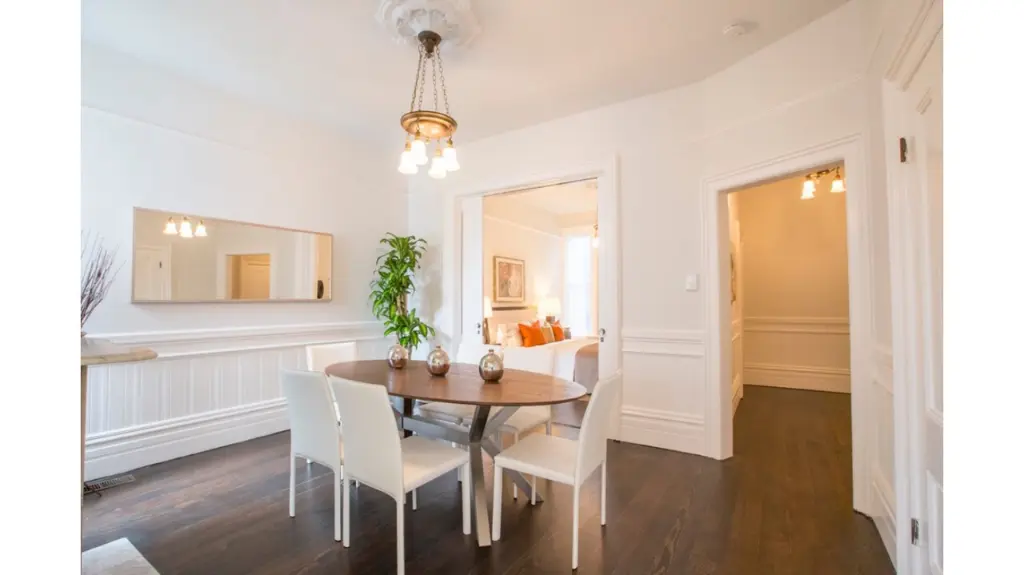 Bright dining room with a round wooden table, white chairs, chandelier lighting, and dark hardwood floors