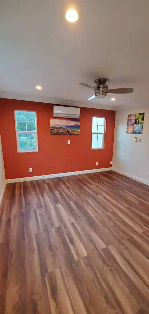 Empty room with orange accent wall, wood flooring, ceiling fan, recessed lighting, wall-mounted air conditioner, and windows