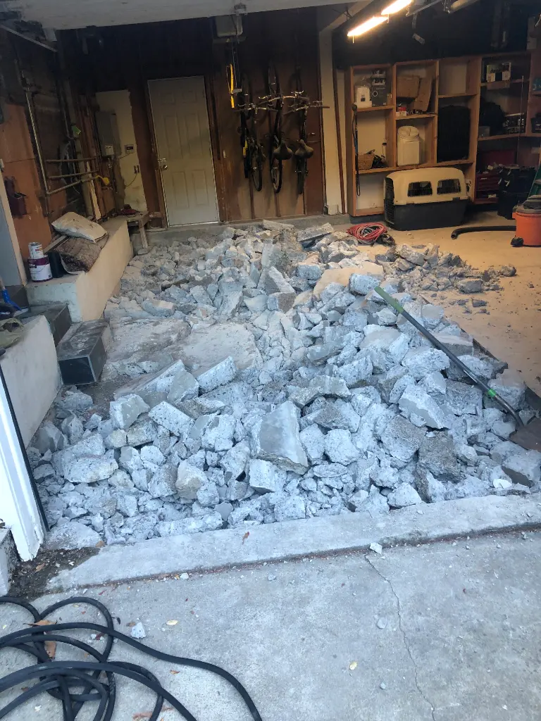 Garage interior with piles of broken concrete slabs covering the floor during an active demolition project