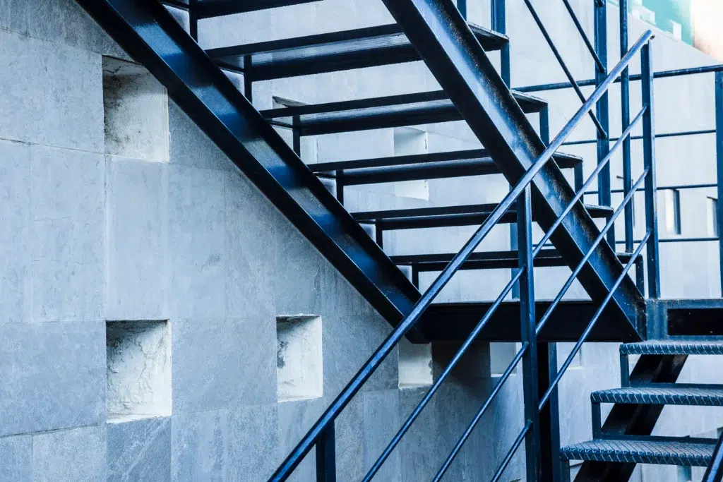 Industrial metal staircase with black steel frame and railings against a gray concrete wall.