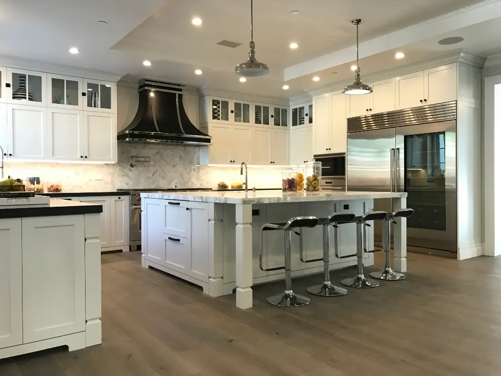 Luxury kitchen with large marble island, stainless steel appliances, and white cabinetry under pendant lights.