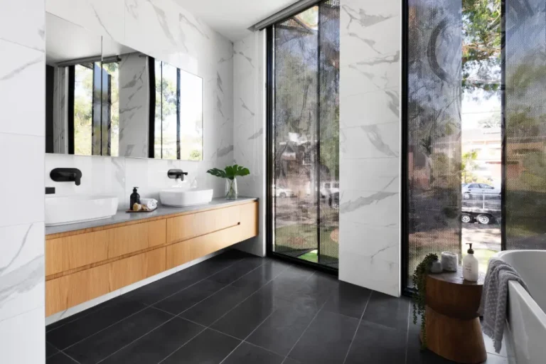 Modern bathroom with marble walls, floating wood vanity, vessel sinks, and full-height windows with perforated screens