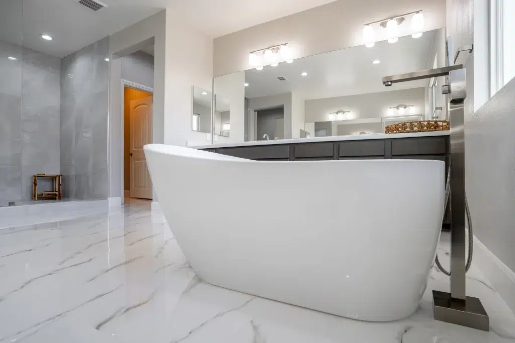 Modern bathroom with freestanding white bathtub, marble floor, large vanity mirror, and glass walk-in shower.