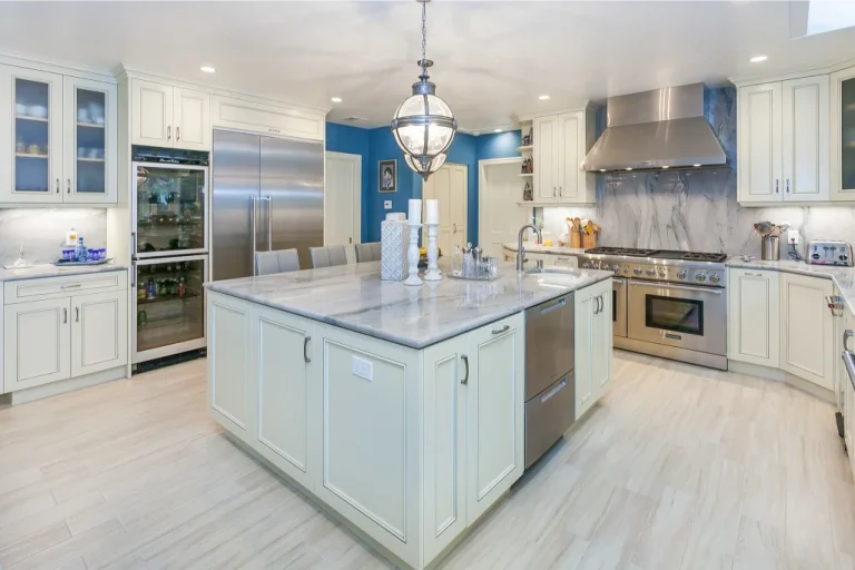 Modern kitchen with marble island, stainless steel appliances, and white cabinetry under bright lighting.