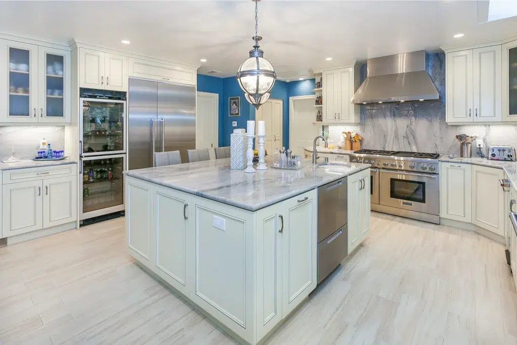 Modern kitchen with marble island, stainless steel appliances, and white cabinetry under bright lighting.