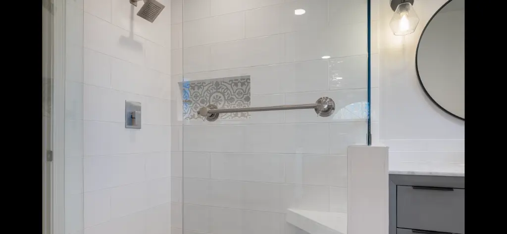 Modern walk-in shower with white tile walls, glass panel, towel bar, and patterned accent tile