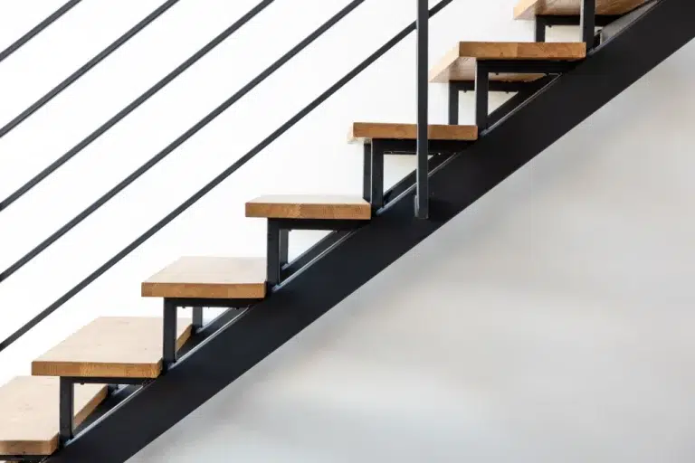 Modern staircase with wooden steps and black metal frame against a white wall.
