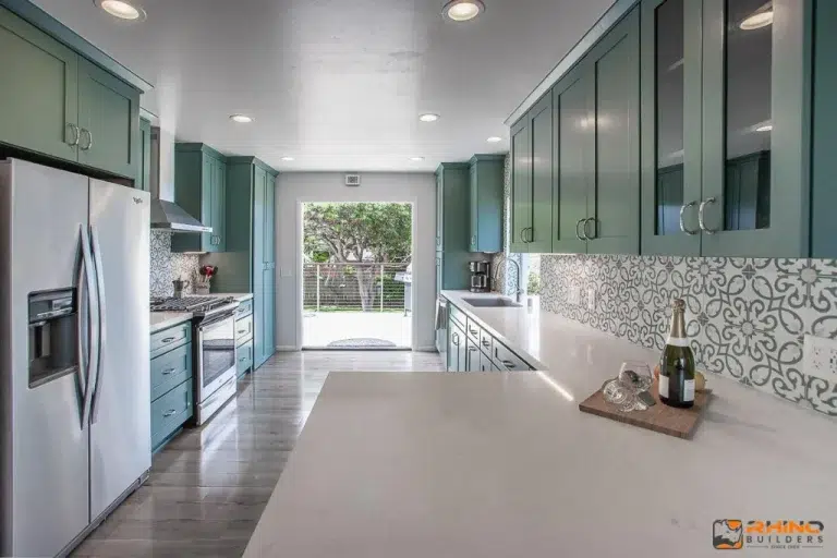 Contemporary kitchen with teal cabinets, patterned tile backsplash, stainless steel appliances, and quartz countertops.