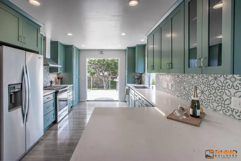 Contemporary kitchen with teal cabinets, patterned tile backsplash, stainless steel appliances, and quartz countertops.
